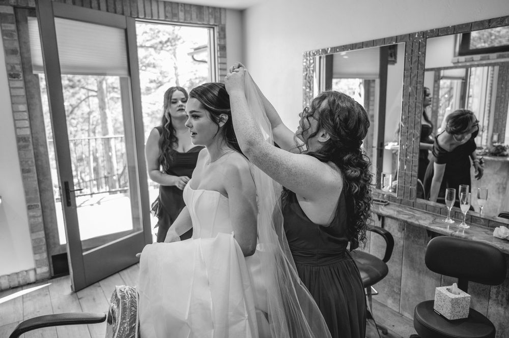 Bridesmaids helping bride with veil in bridal suite, black and white wedding preparation photo.