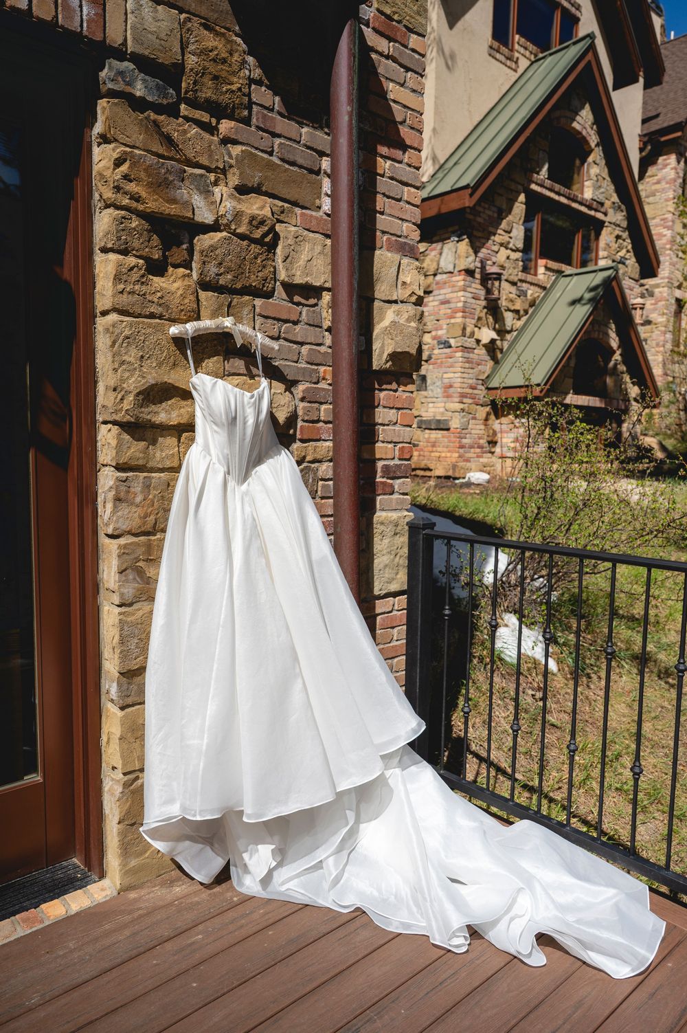 White wedding dress hanging on a rustic stone building balcony with a flowing train on a sunny day.