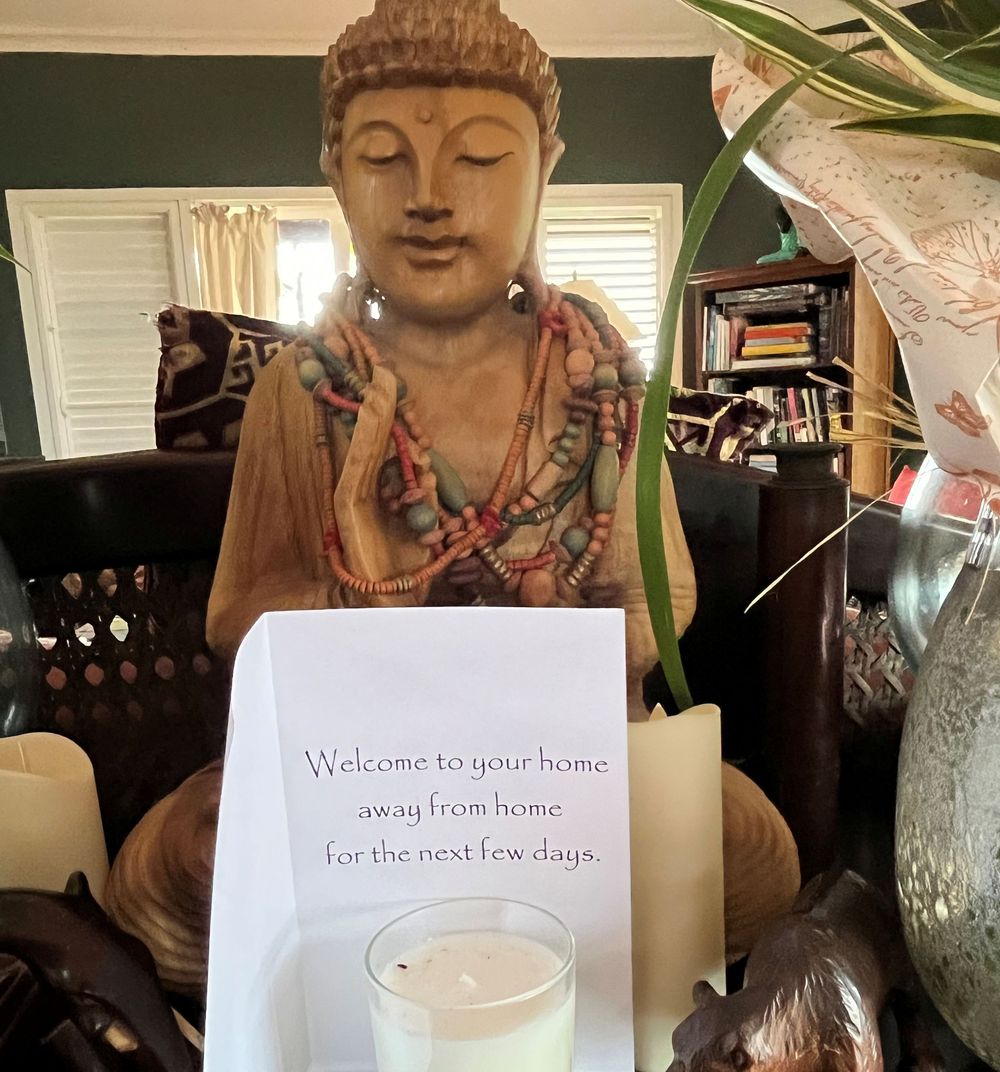 Buddha statue with welcome home sign and candle in a cozy, decorated living room setting.