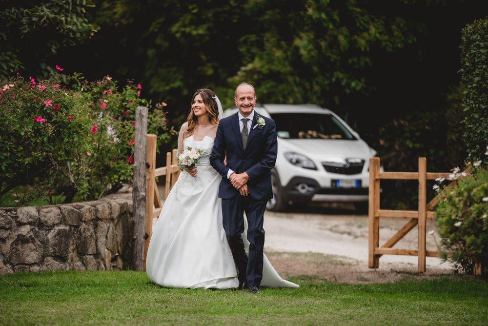 Wedding couple posing by rustic wooden gate and stone wall in garden setting.