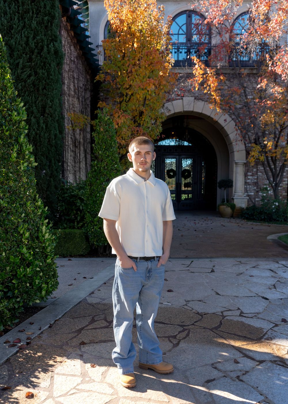 Young man in white shirt and jeans standing in front of elegant stone building with arched entrance.