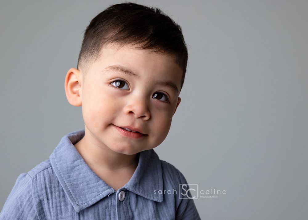 Smiling young boy with dark hair wearing a blue collared shirt, portrait photo by Sarah Celine Photography.