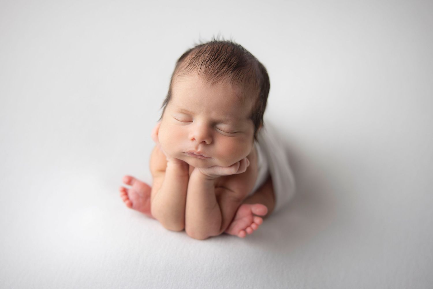 Sleeping newborn baby wrapped in teal swaddle inside a small bucket with a green pillow.