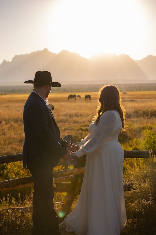 Bride and groom holding hands at sunset with Grand Teton mountains and golden fields in background.