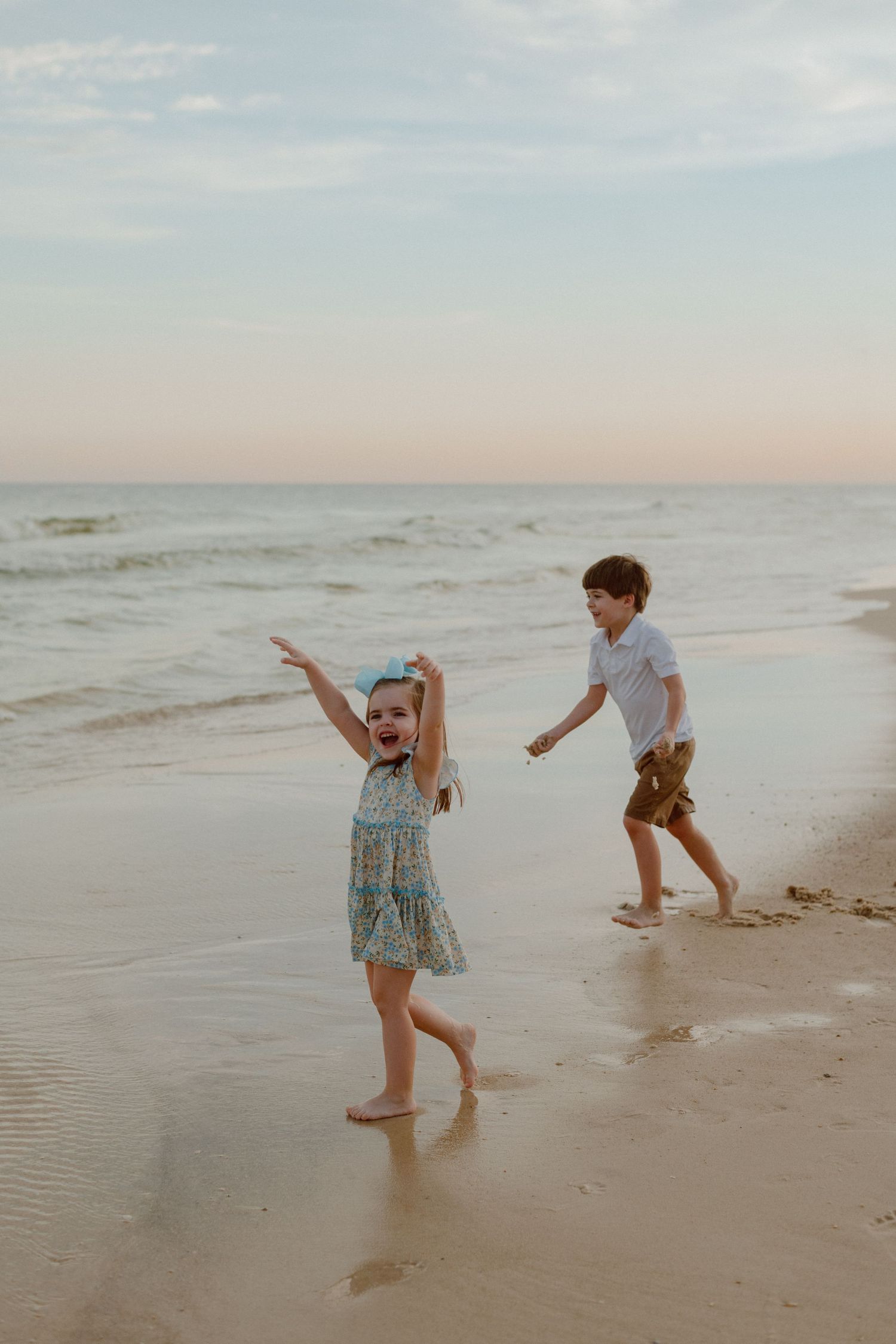Two children playing and laughing together on beach at sunset.