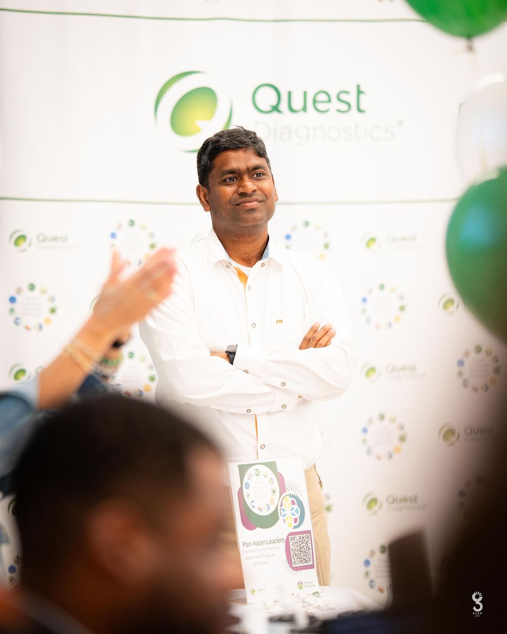 A blurred corporate event backdrop with a green Quest logo visible in the background.
