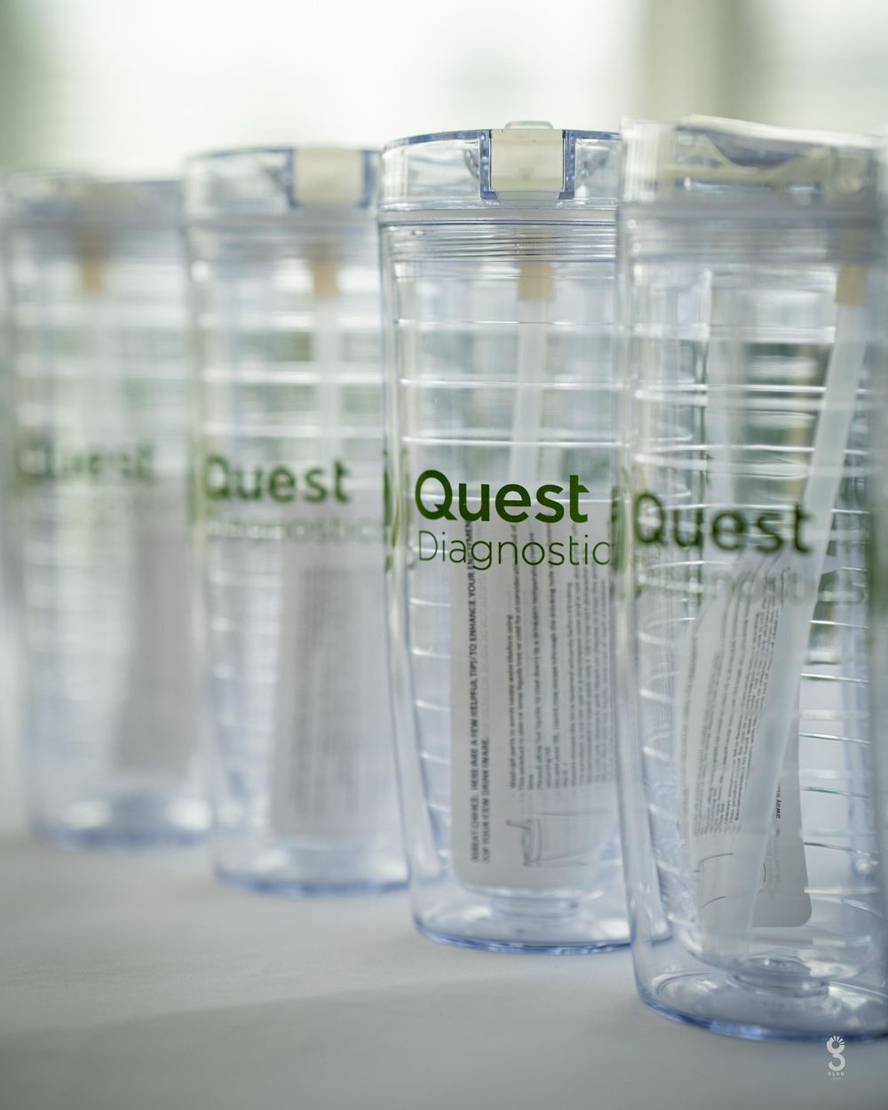 Clear plastic Quest Diagnostic collection containers lined up in a row with green labeling.