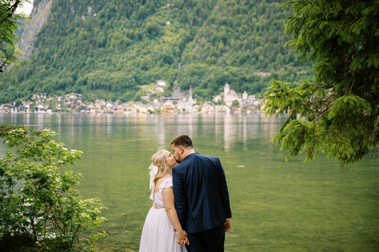 A romantic moment by an Alpine lake with mountain village and forest scenery in background.