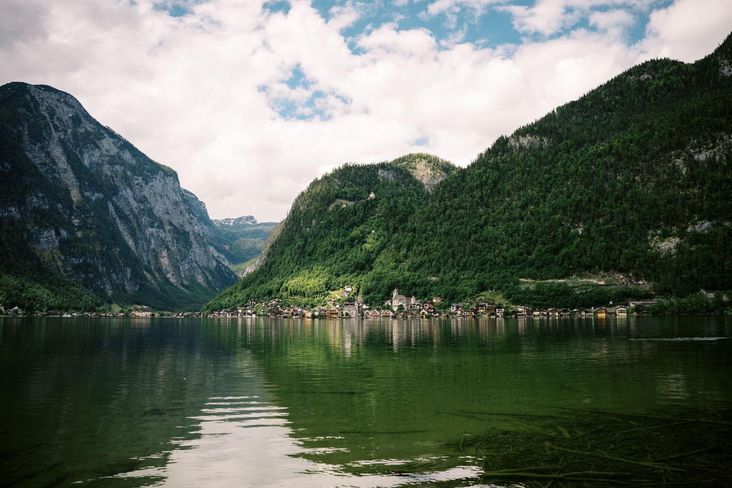 Scenic view of Hallstatt village nestled between mountains along emerald green lake in Austrian Alps.