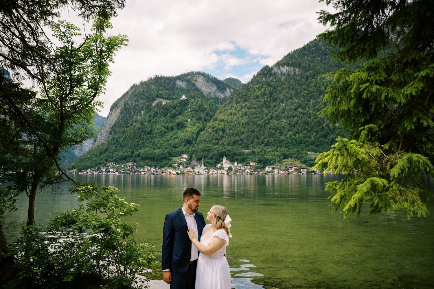 Couple enjoying scenic mountain views beside emerald green lake in Austrian Alps with village in distance.