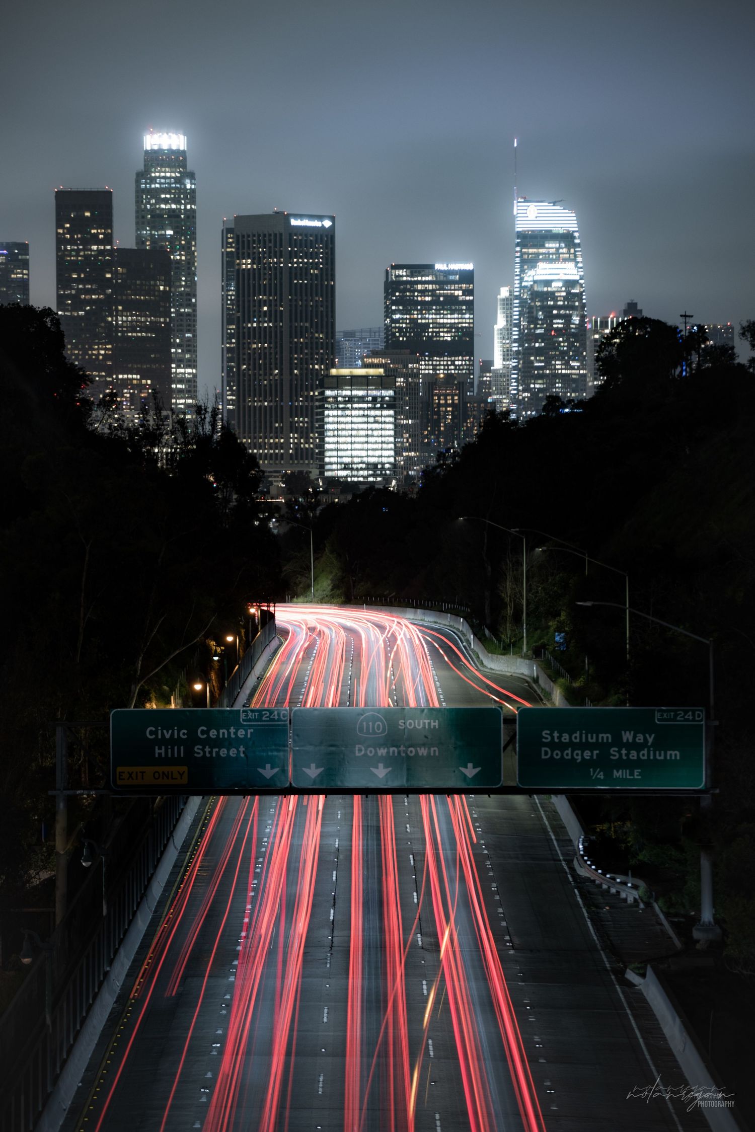 Los Angeles skyline at night with light trails from cars on the highway leading to downtown.