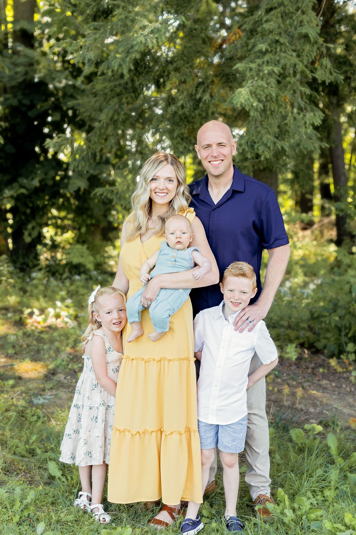 Family of five poses outdoors for portrait against lush green forest background.