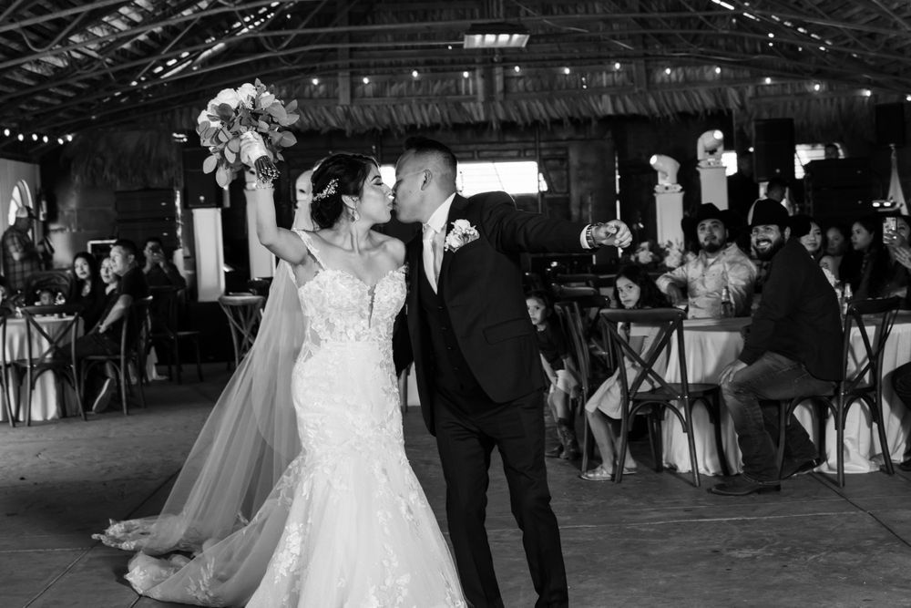 A couple shares their first dance at a rustic barn wedding reception surrounded by guests and string lights.
