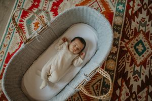 Sleeping baby in cozy gray lounger lies on ornate patterned area rug with bohemian designbromley and Beckenham newborn photography