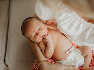 A tiny newborn baby wearing a white diaper rests peacefully against a soft textured surface.