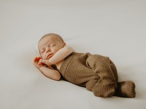A sleeping baby wearing a brown knit sweater lies peacefully on a white background.