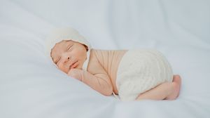 Peacefully sleeping newborn wearing soft pink outfit curled up on white background.