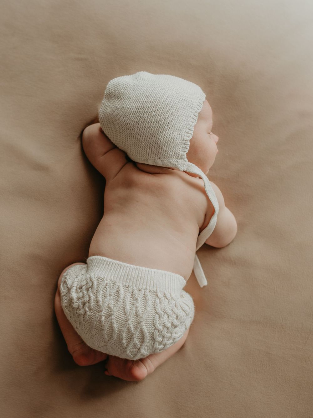 Newborn baby wearing white knit clothing lies on beige blanket showing different resting poses in a series.