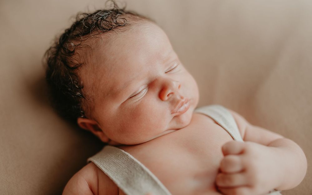 A sleeping newborn baby swaddled in white fabric rests peacefully on soft bedding.