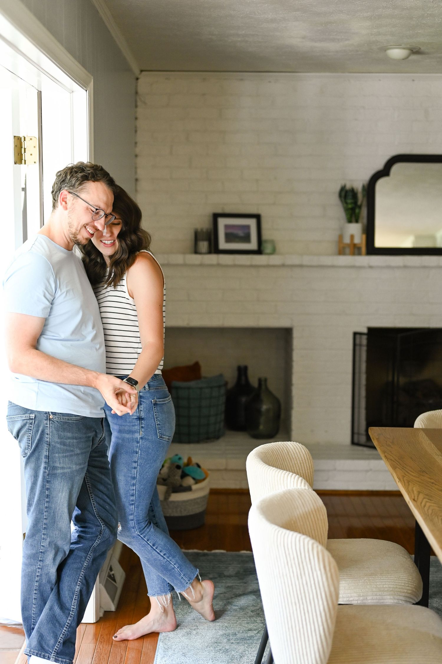 Casual couple embracing in modern living room with white brick fireplace.