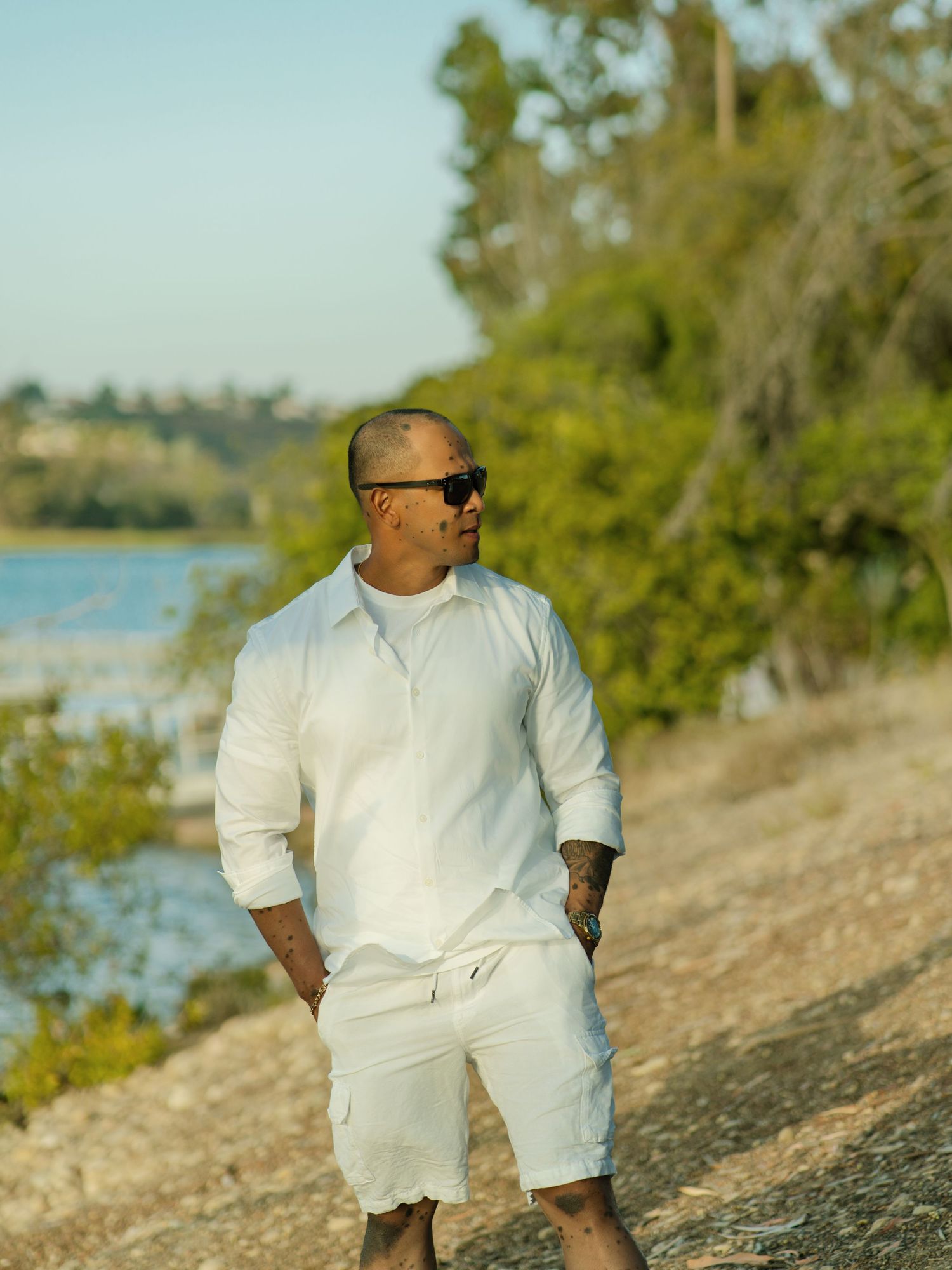 Person in all-white outfit standing on hiking trail near waterfront on sunny day.