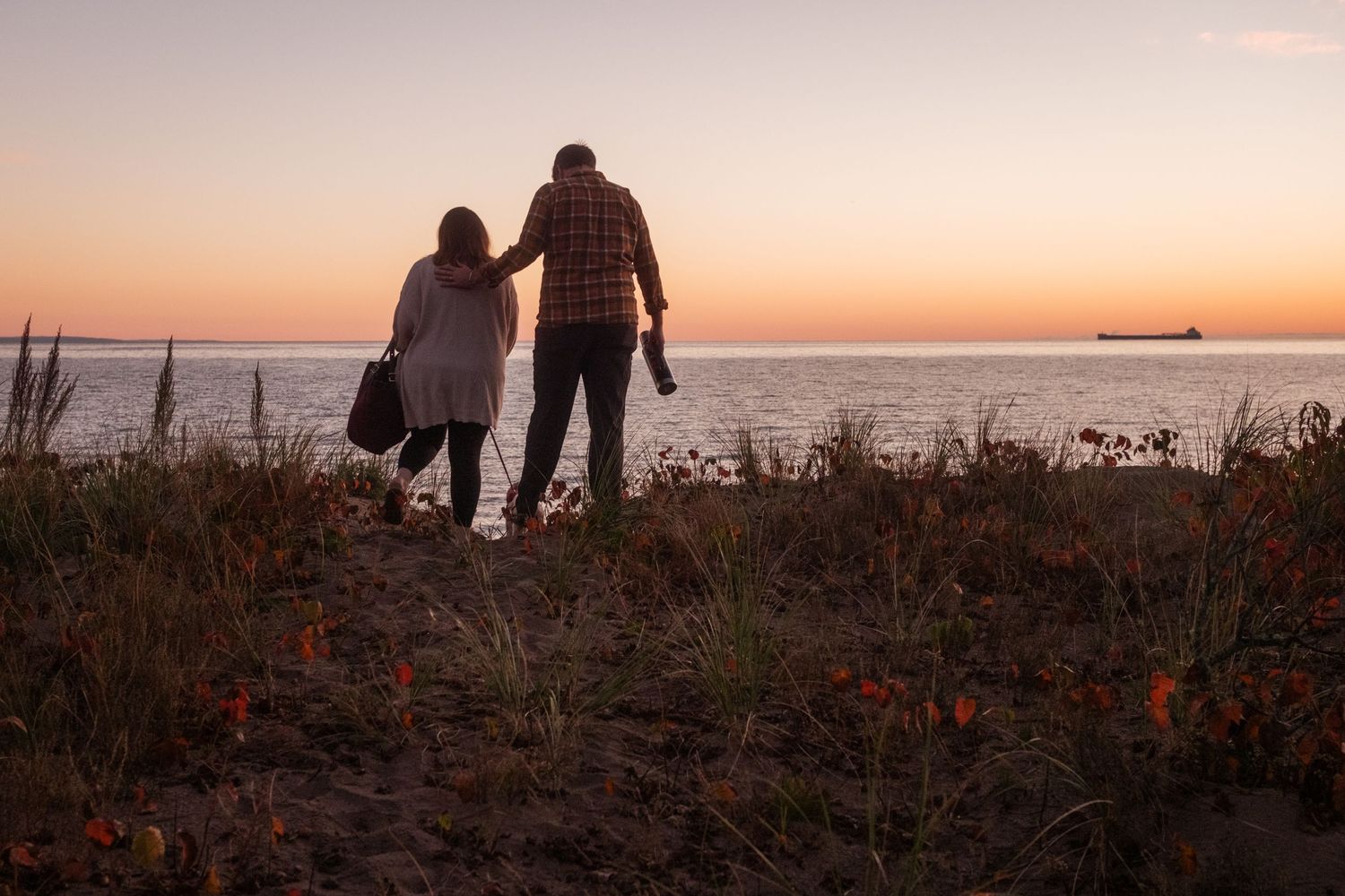 Two silhouetted figures stand together watching a sunset over the ocean horizon.