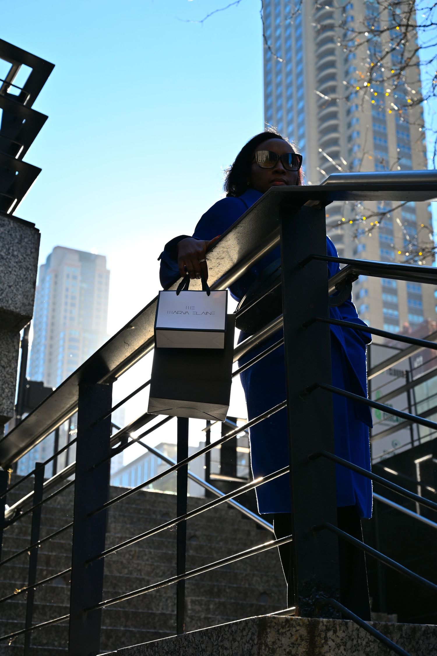 A person in blue stands on urban steps against a backdrop of tall city buildings during daytime.