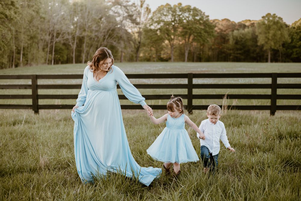 A family in light blue dresses twirls and plays together in a grassy field at sunset.