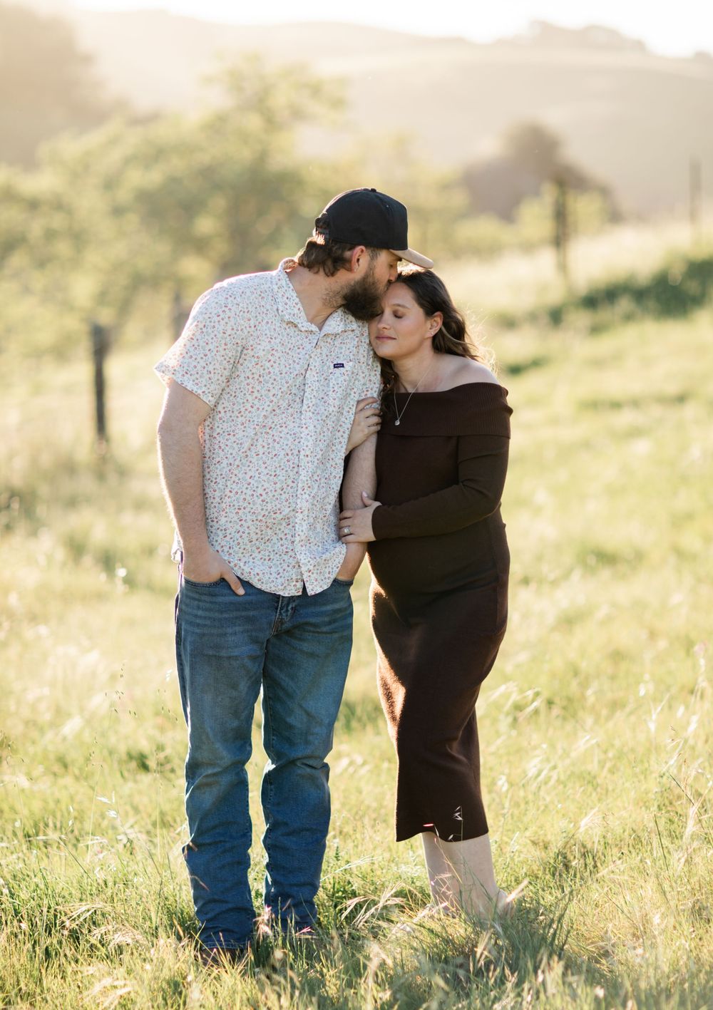 A couple shares an intimate moment together in a sunlit meadow with golden grass and soft lighting.