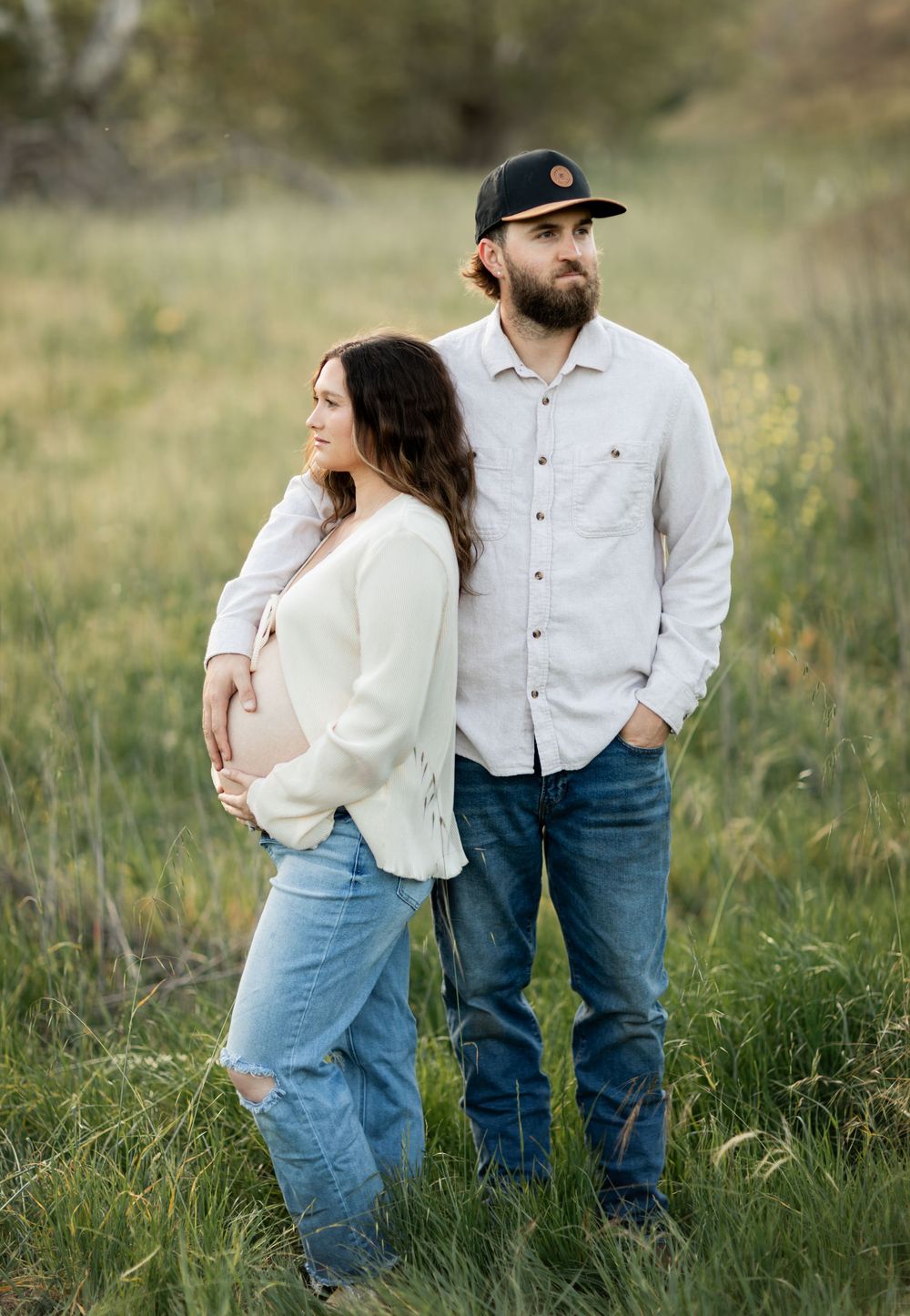 Couple in casual attire standing close together in a grassy meadow during a romantic outdoor photoshoot.