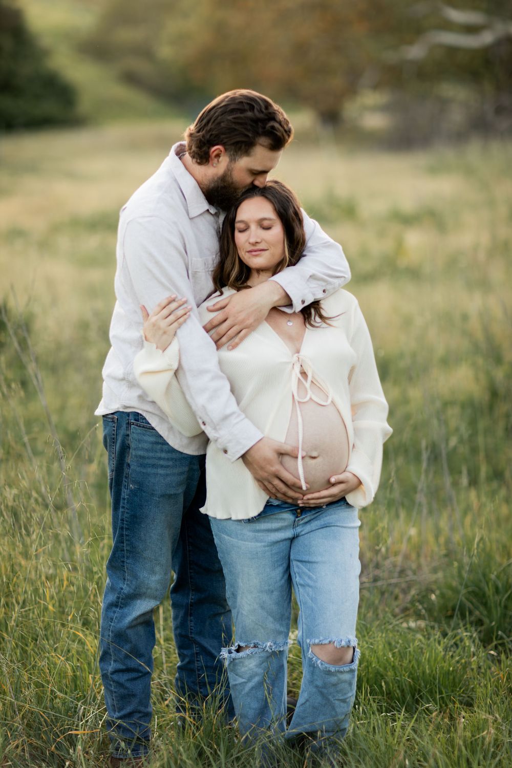 Intimate maternity photos showing couple embracing in a natural outdoor setting with tall grass and warm lighting.