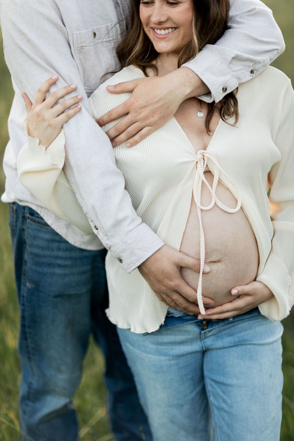 A couple in jeans and white shirts embrace while sharing a tender moment during an outdoor maternity photoshoot.
