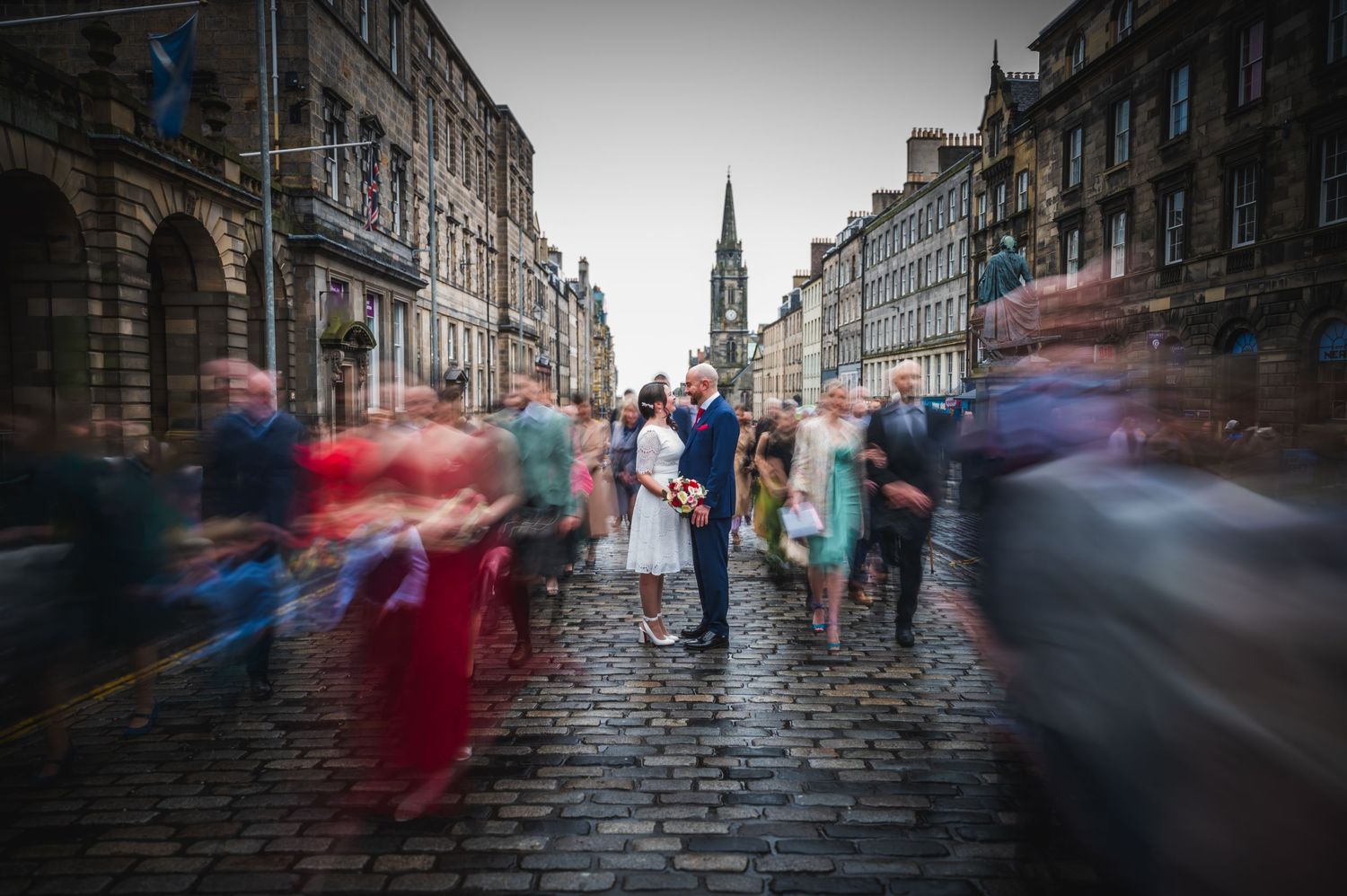 Motion blur of people walking on a historic cobblestone street in Edinburgh with church spire in background on the Royal Mile.