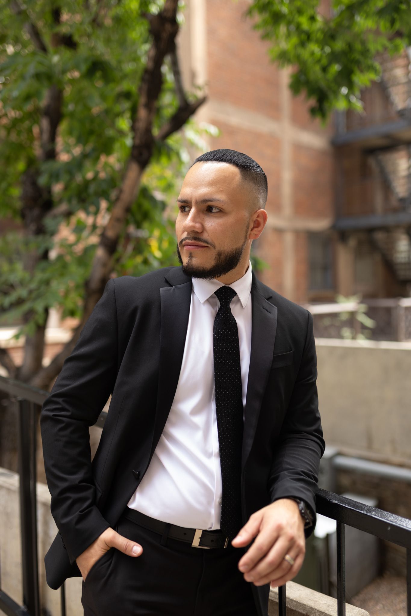 Man leans agains the fence in a tux posing for a photo