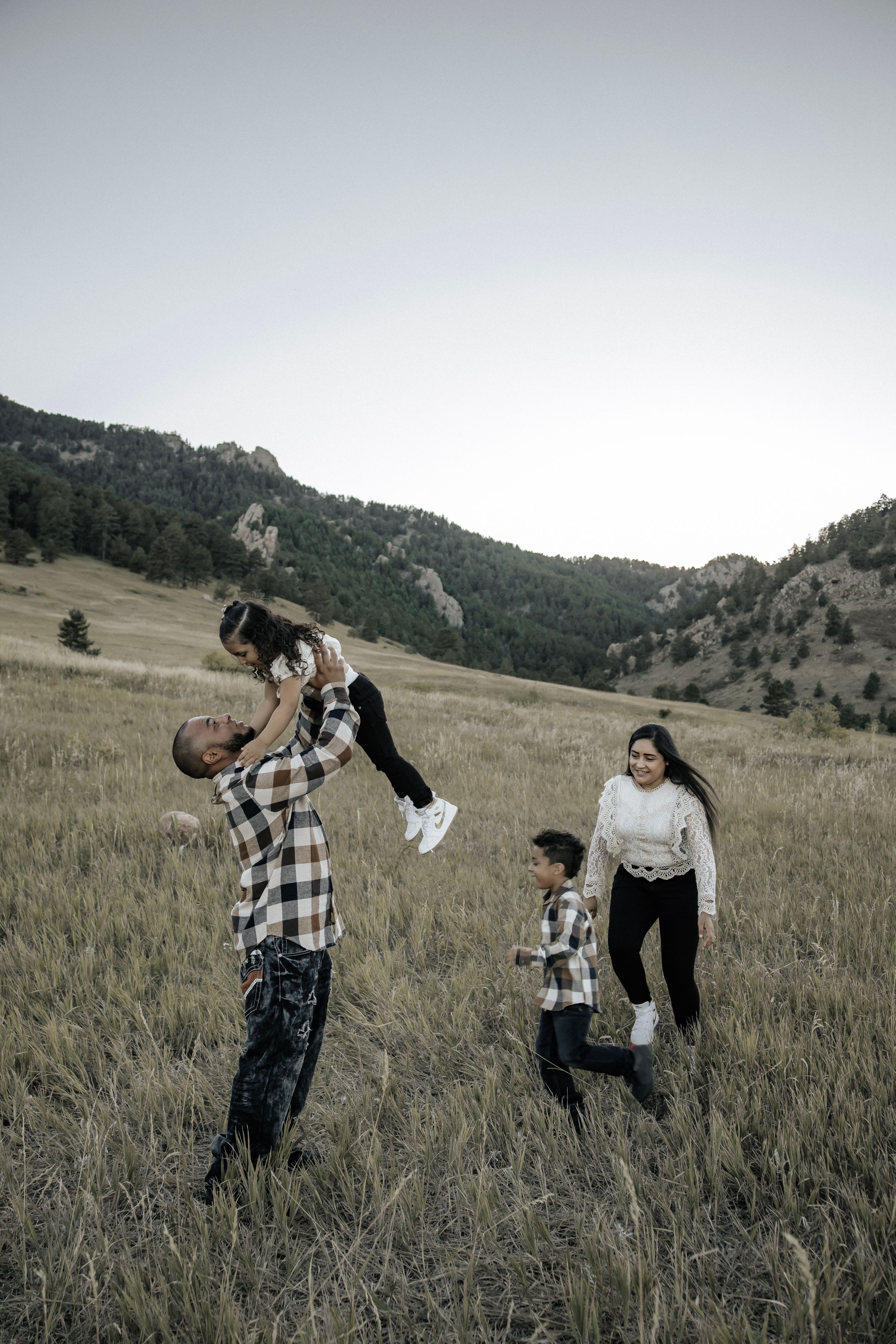 Dad tosses young daughter in the air playfully, while mom chases after son
