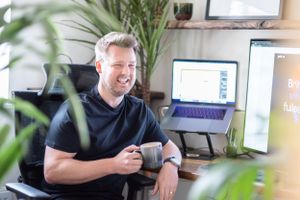 Professional working from home at desk setup with laptop stands, plants and office equipment in bright workspace setting.