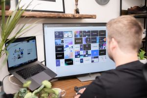 Person working at desk with multiple computer screens displaying design layouts and digital content.
