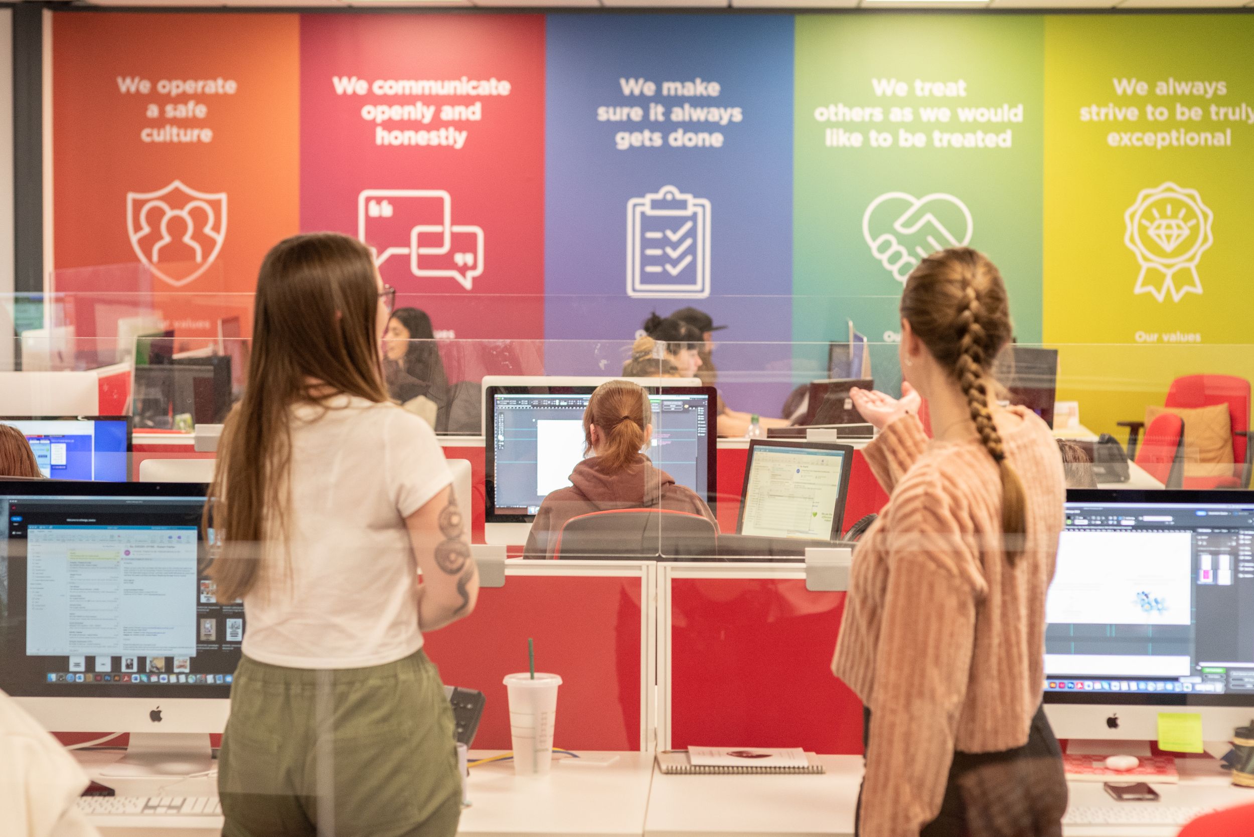 Students interact with staff at a colorful service desk featuring motivational banners and computer workstations.