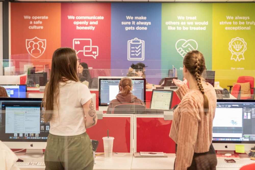 Students interact with staff at a colorful service desk featuring motivational banners and computer workstations.