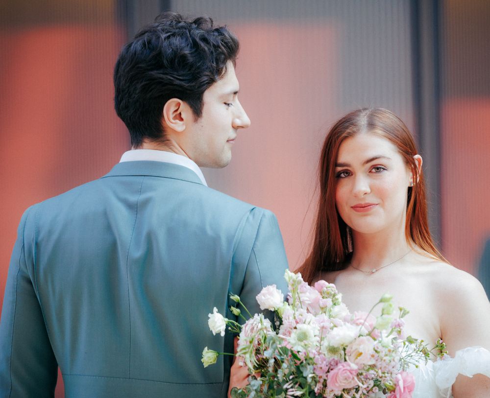 A bride holding a pink bouquet gazes at her groom in a teal suit during a wedding shoot.