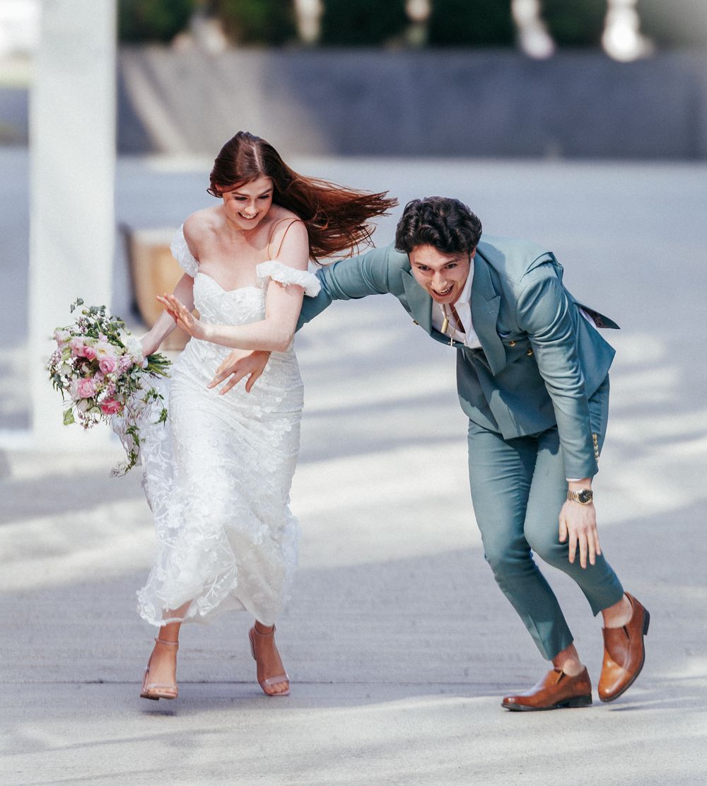 A laughing bride and groom playfully pose outdoors during a fun and candid wedding photo session.