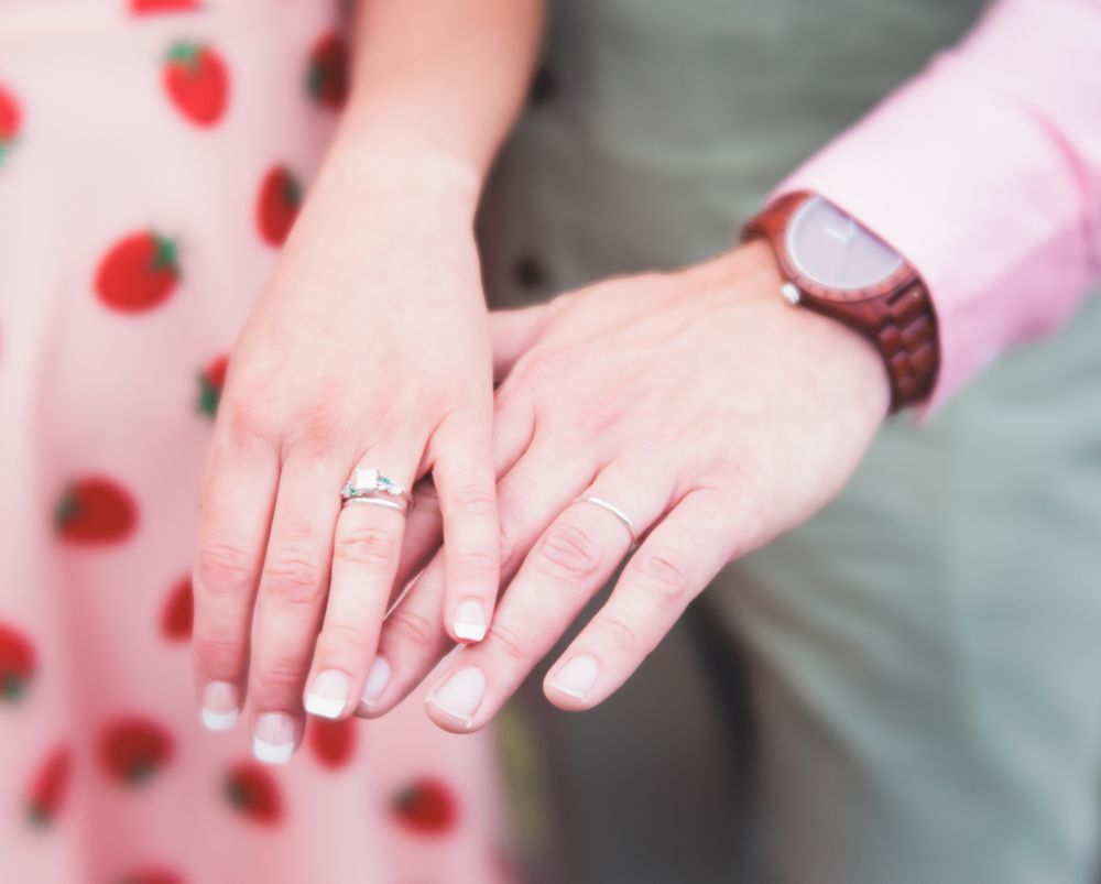 Close-up of couple's hands showing engagement ring and wooden watch, symbolizing love and commitment.