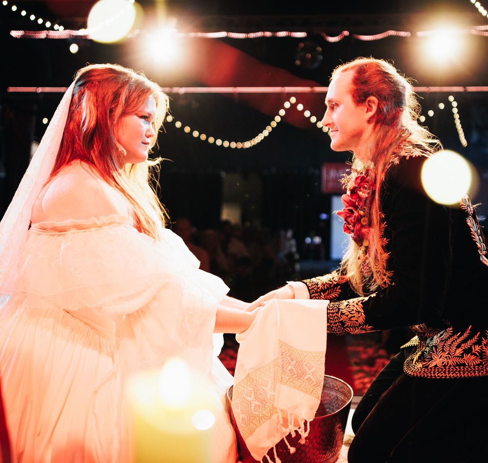 Couple in fantasy wedding attire exchanging vows by candlelight at decorated venue.