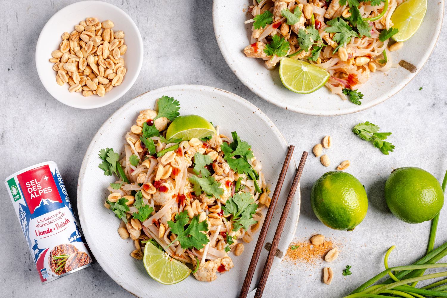 Spicy Thai shrimp salad with crushed peanuts, lime wedges, and fresh herbs arranged on white plates.