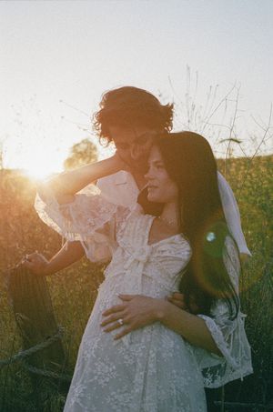 Couple embracing in golden sunset light in a field, bride in lace dress with veil.