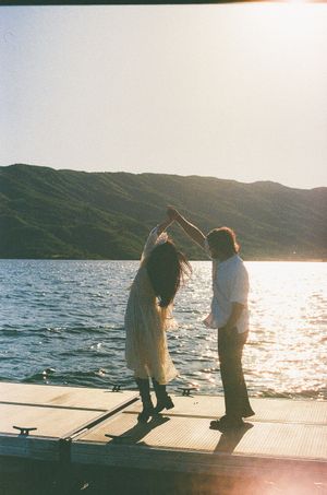 Couple dancing on a wooden dock at sunset with a mountain lake backdrop.