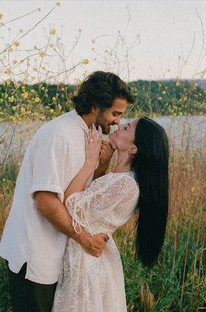 Couple embracing and smiling in a field of yellow wildflowers at golden hour.