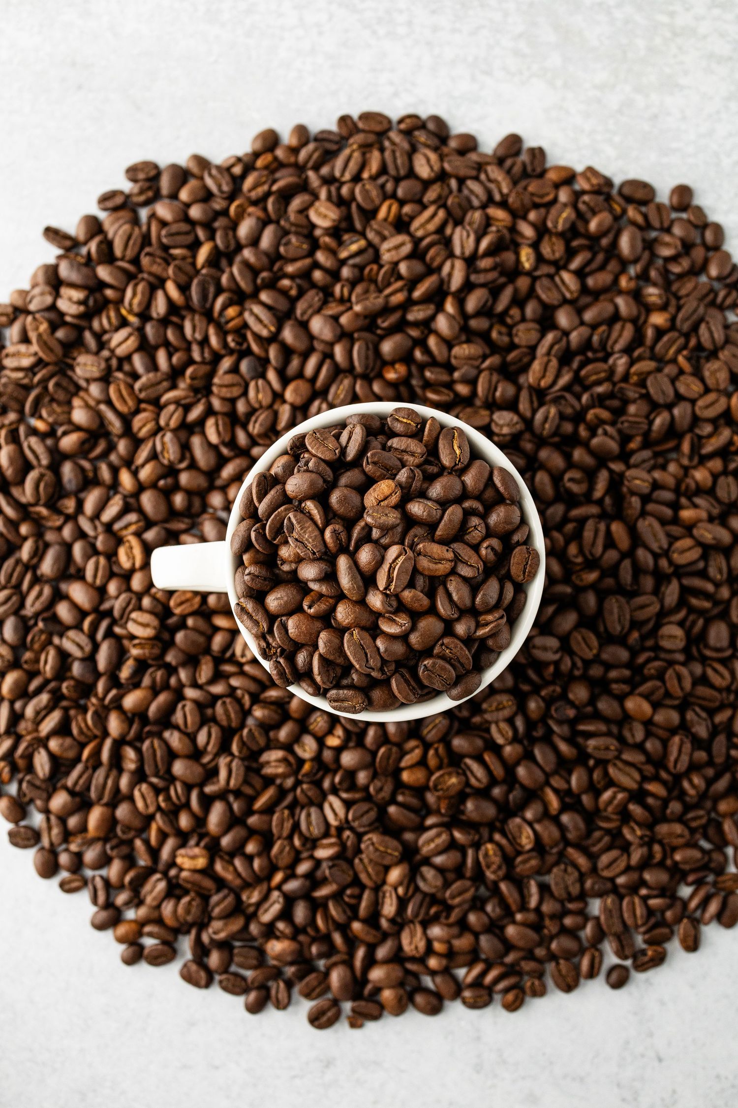 Overhead photo of a pile of Colombian coffee beans with a coffee cup overflowing with more beans in the center by Bella Priscilla Photo NBTX