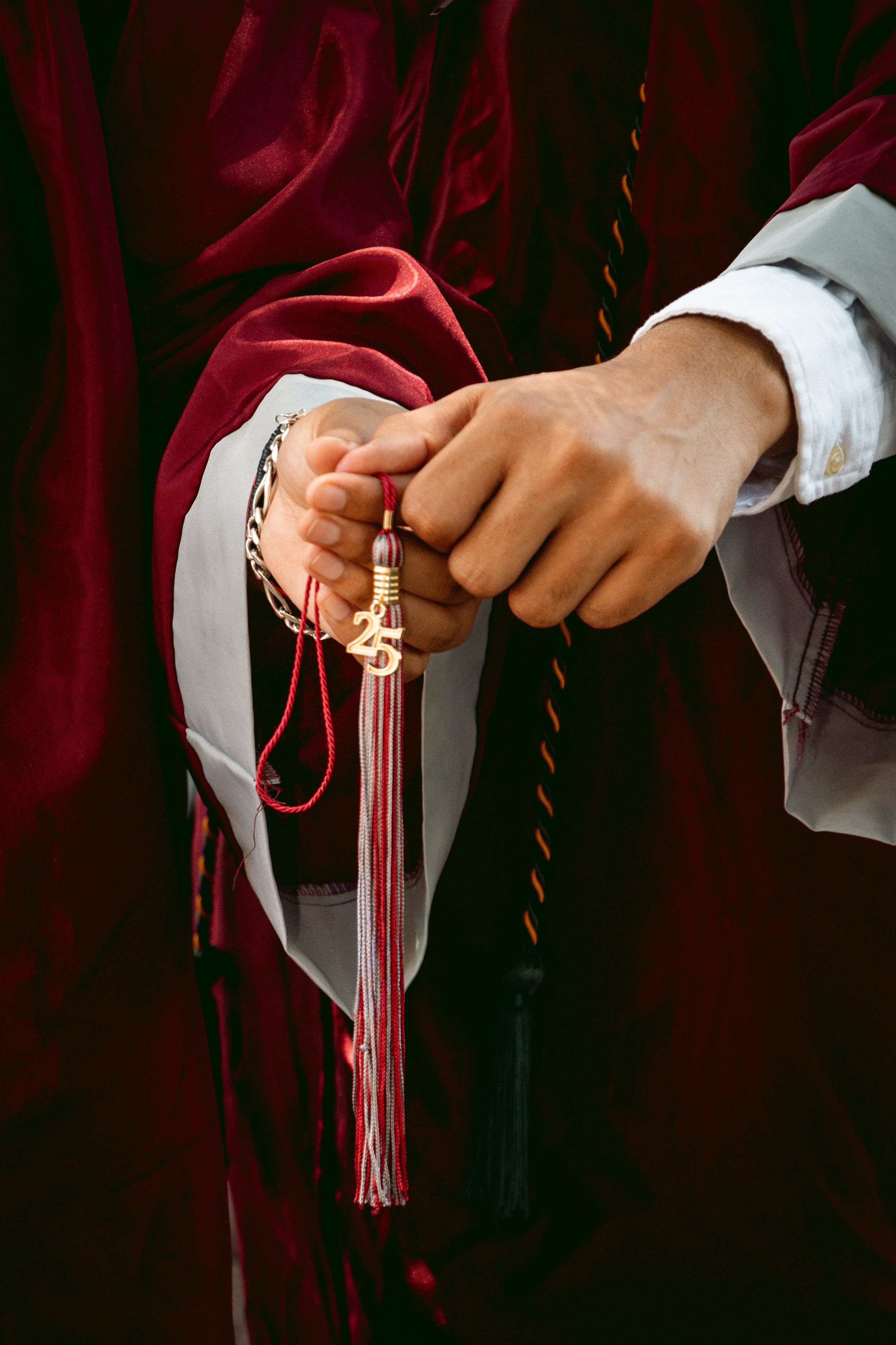 Hands holding a red and gold tassel on a graduation gown during a ceremony.