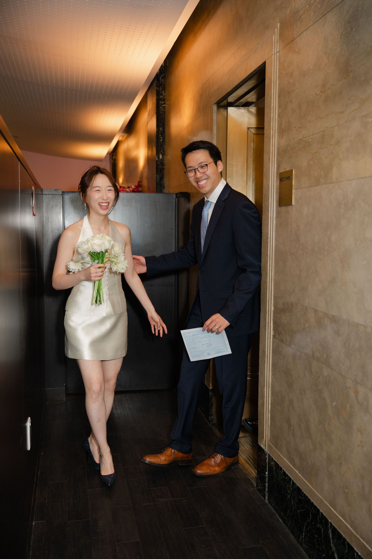 Joyful couple celebrating their wedding at NYC city hall, holding marriage certificate and bouquet, smiling after eloping.